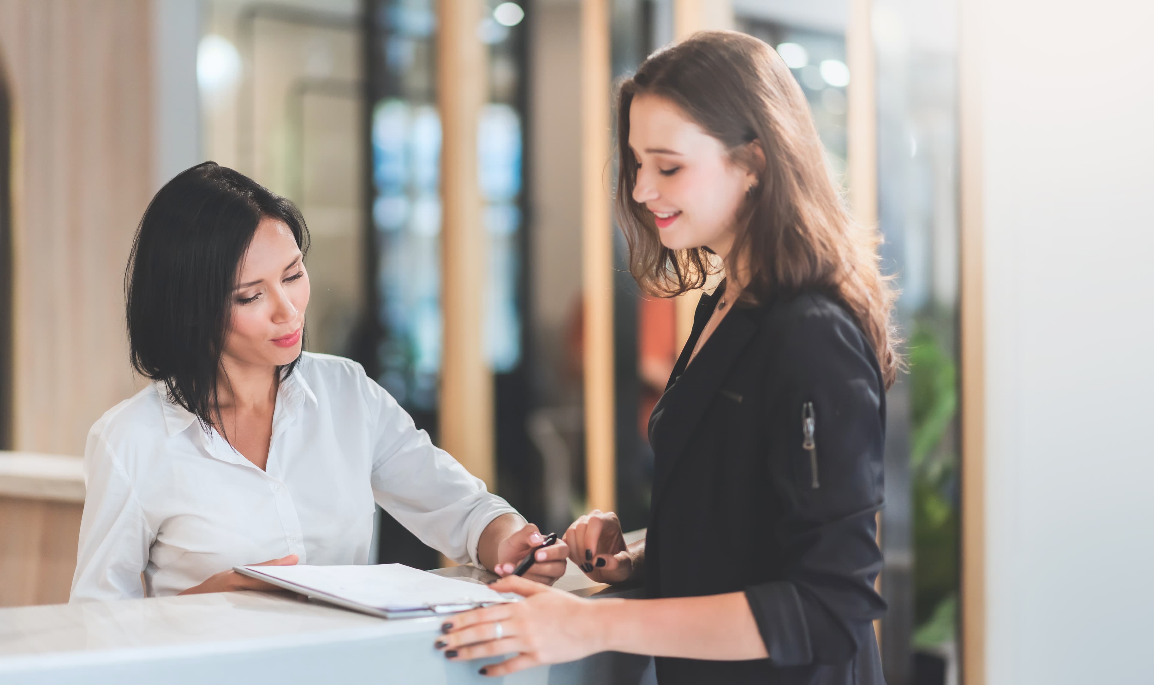 Two women at a receptionist desk looking at papers