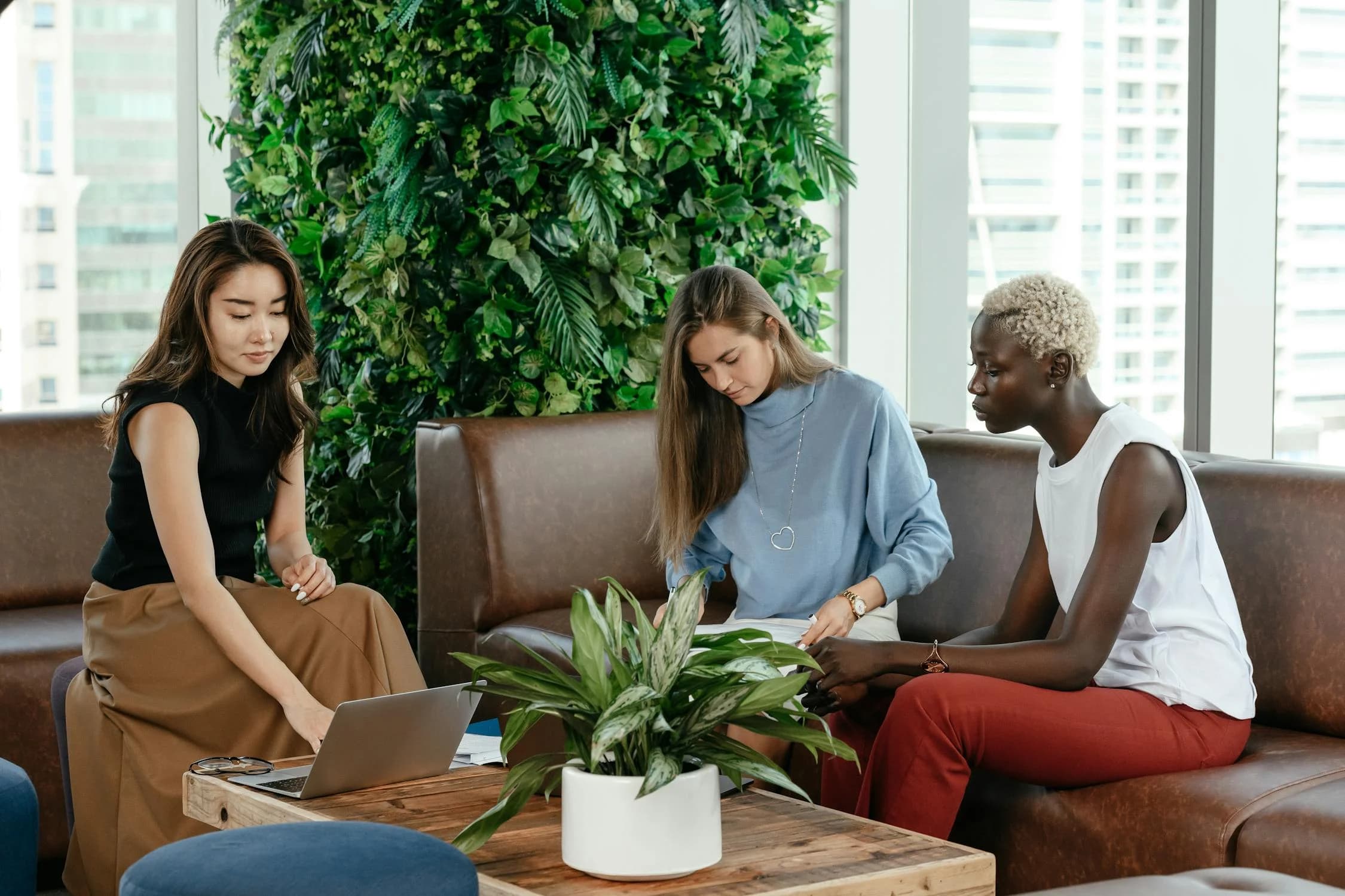 Three women sitting on a couch with laptops working