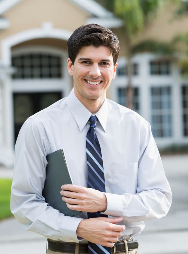 Man smiling in a tie in front of a house