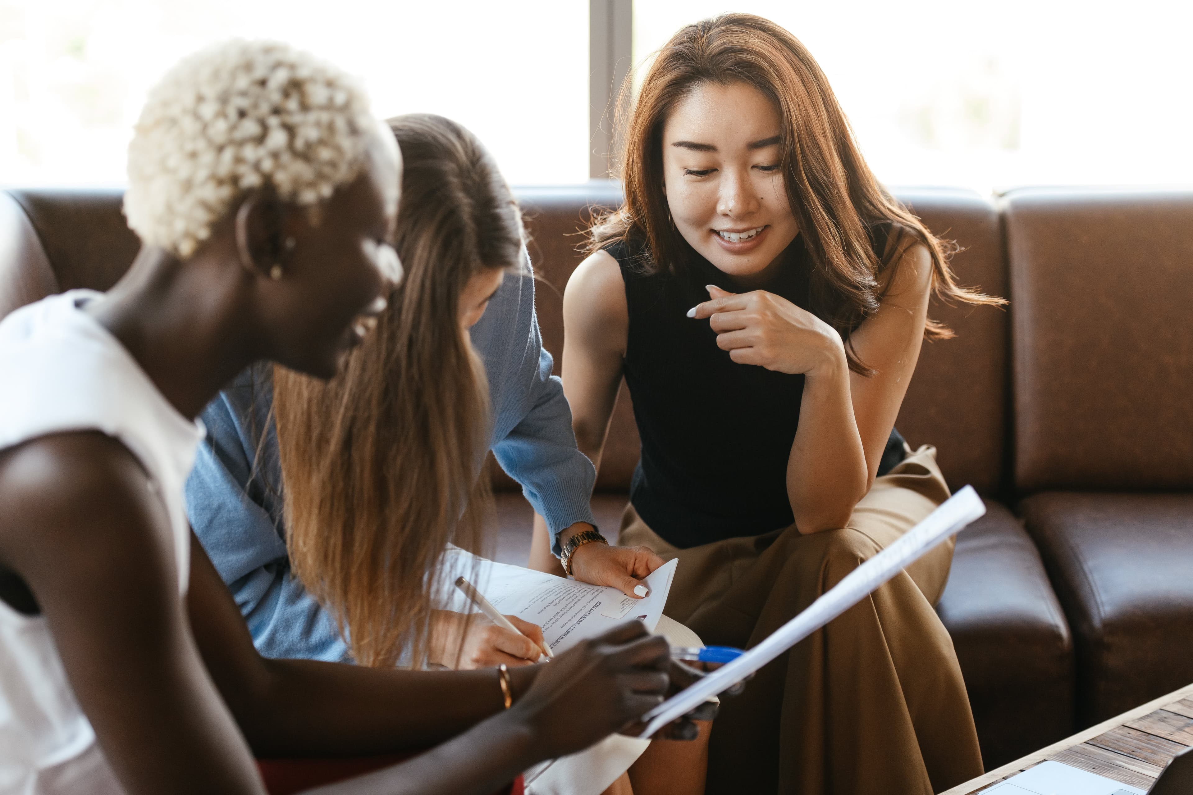 Three women siting on a couch smiling looking at documents