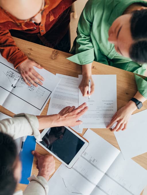 Overhead photo of three people looking at documents spread out on a desk