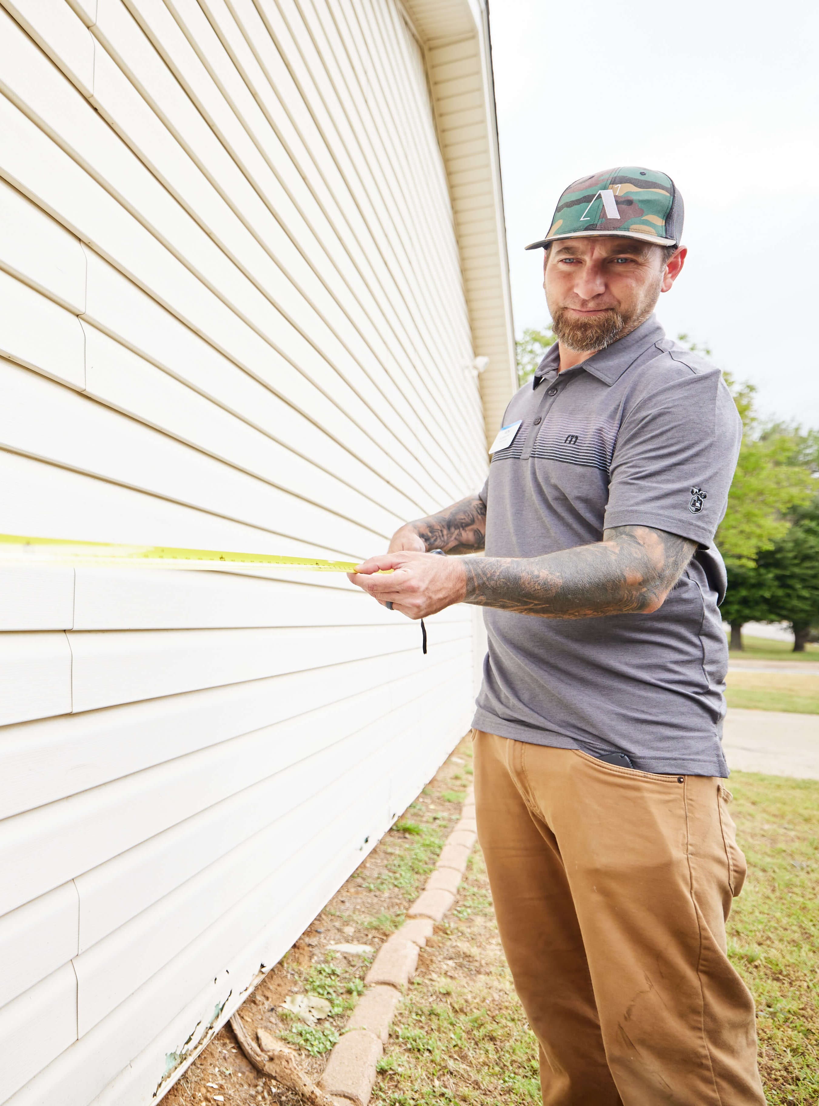 Photo of a man using a measuring tape outside of a house